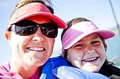 A five year old girl smiles while wearing a pink visor and a life jacket. Her mother smiles too while wearing a red visor, Bear Lake, Utah.