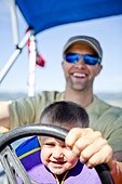A man pilots a pontoon boat while his three year old son helps steer, Bear Lake, Utah
