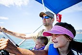 A man pilots a pontoon boat while his three year old son helps steer, and his five year old daughter sits next to them, Bear Lake, Utah.
