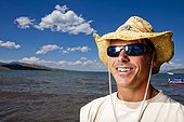 A man smiles in a straw hat as he stands for a portrait on the shores of Bear Lake, Utah.