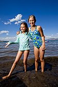 Two middle school aged sisters in bathing suites stand on the shores of Bear Lake, Utah.
