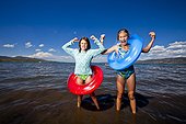 Two middle school aged sisters in bathing suites stand on the shores of Bear Lake with red and blue inner tubes, Utah.