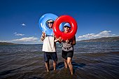 A man and a woman stand with a red and blue inner tube for portraits on the shores of Bear Lake, Utah.