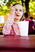 An eight year old girl, eats ice cream while sitting at red picnic table, Garden City, Utah.
