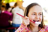An eight year old girl, eats ice cream while sitting at red picnic table, Garden City, Utah.