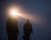 Two climbers use a headlamp to perform evening tasks in a whiteout.
