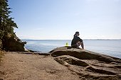 A woman sits on sandstone on the coastline of Larrabee State Park.