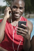 Portrait of male athlete smiling and listening to music on smart phone, Barcelona, Spain