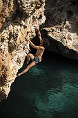 Man doing psicobloc in Mallorca, Spain. Psicobloc is a rock climbing discipline where the climber climbs without rope and other safety gear on selloffs, going into the water in case of fall.