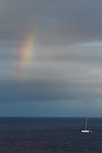 Rainbow on cloudy sky over sailboat drifting on calm sea waters, Bali, Indonesia