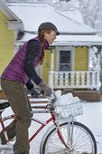 Adult woman riding bicycle and transporting pile of snowballs in basket, Sandpoint, Idaho, USA