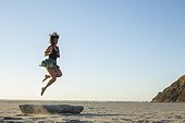 Adult woman jumping off a log at the beach and turning around in the air to face the camera. Cape Disappointment State Park, Washington.