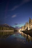 Aurora Borealis at night over lake with silhouette of man standing on shore, Banff National Park, Alberta, Canada