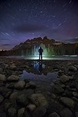 Man standing on lakeshore at night near Castle Mountain, Banff National Park, Alberta, Canada