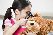 Girl examining teddy bear with otoscope