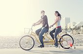 Couple riding tandem bike on beach boardwalk