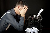 agonized writer. young man in his thirties sitting frustrated behind a classic typewriter