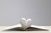 Two pages in open book creating a heart. Still life of open hardback book lying on a surface with two middle pages creating the shape of a heart
