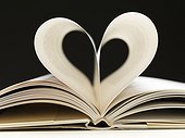 Two pages in open book creating a heart. Still life of open hardback book lying on a surface with two middle pages creating the shape of a heart