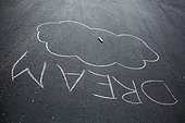 A chalk drawing of the word DREAM.. A chalk drawing on a driveway of the word Dream with a cloud.
