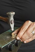 Close up detail of silversmith's hands using a hammer and anvil to shape sterling silver jewelry