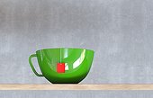 Close-up of a green cup of tea, with a red teabag-label, sitting on a wooden table against a concrete wall