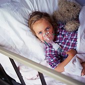 Child in hospital bed, wearing oxygen mask, holding stuffed animal