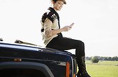 Couple on Roadtrip. young woman sitting on the bonnet of her jeep going through text messages.