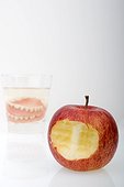 False teeth, dentures in a glass of water beside an apple