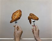 Human hand holding fork with roasted chicken, close-up