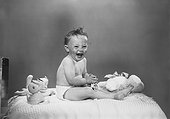 Baby boy sitting on bed with toys, laughing