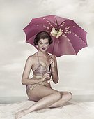 Young woman sitting on beach holding umbrella, smiling, portrait