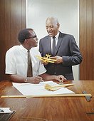 Two businessmen with model aeroplane by table