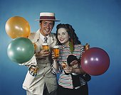 Young couple holding beer glass with balloons and toys, smiling, portrait