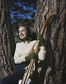 Young woman leaning on tree with skis, smiling
