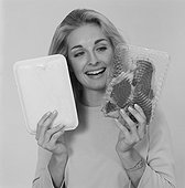 Young woman holding packaged meat against white background, smiling