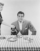 Man sitting at breakfast table, woman pouring black tea in cup
