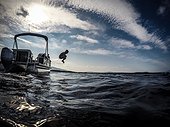 A boy jumps from a pontoon boat into a lake.. Moosehead Lake, Maine, USA.