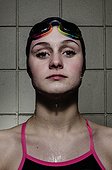 A young female swimmer in a bathing suit, black swim cap, and goggles, poses for a portrait.. Brunswick, Maine, USA.