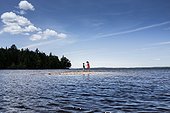 A boy and a girl look at a shell on a sand bar in the middle of a lake.. Moosehead Lake, Maine, USA.
