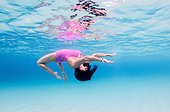 A woman in a pink bathing suit does a back flip in clear blue water.. British Virgin Islands.