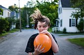A young boy lets the air out of an orange balloon.. Bath, Maine, USA.
