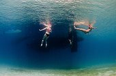 Two women in bikinis float in the water near the back of a boat.. British Virgin Islands.