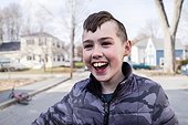 A boy laughs while standing in the street.. Bath, Maine, USA.