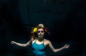 A young woman wearing goggles with flowers in her hair looks at the camera in a dark swimming pool.. Brunswick, Maine, USA.