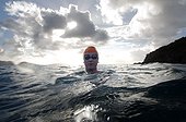 A woman in goggles and an orange swim cap looks at the camera while treading water.. British Virgin Islands.