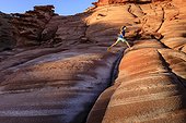 A girl leaps over cracks in a red sandstone formation on the Baja Peninsula, at Puerto Gato.. Puerto Gato, Baja California, Mexico.