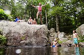 A girl in a bathing suit leaps from a rock into the water below.. Sanford, Maine, USA.