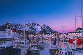 Norway, Nordland, Lofoten Islands, Scandinavia, Henningsvaer, The fishing village of Henningsvaer at duskwith the boats in the harbor and the snow capped mountains in the background