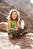 Portrait of smiling girl with water bottle sitting on rock
